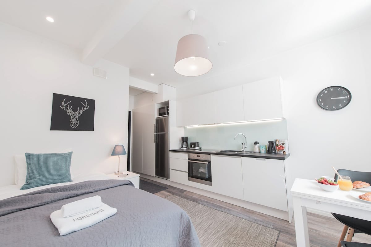 Une chambre d’hôtel moderne équipée d’un lit, d’une petite table avec des articles pour le petit-déjeuner, d’une kitchenette et d’une horloge murale.