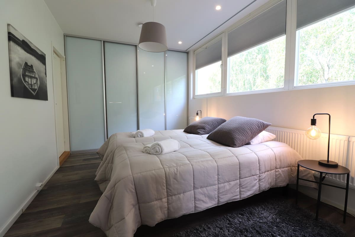 Une chambre à coucher avec un lit, une table de chevet, une lampe, une fenêtre et une porte.