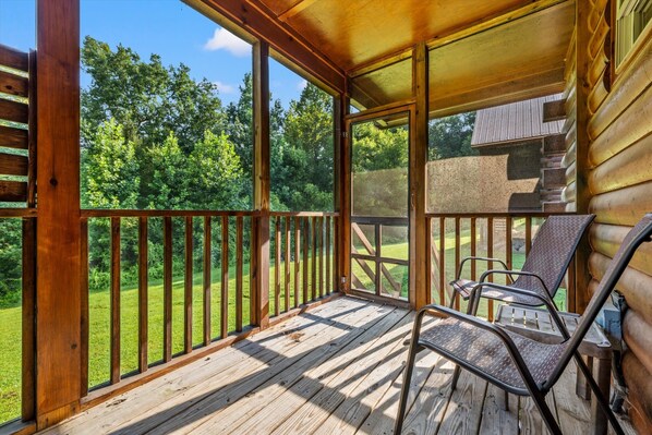 A wooden deck with a railing, a covered area with a window, and a chair.