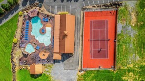 Eine Vogelperspektive zeigt ein Resort mit mehreren Schwimmbecken, einem Tennisplatz und verschiedenen Liegebereichen.