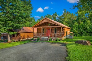 A log cabin with a red door, a porch, and a stone staircase leading up to the entrance.