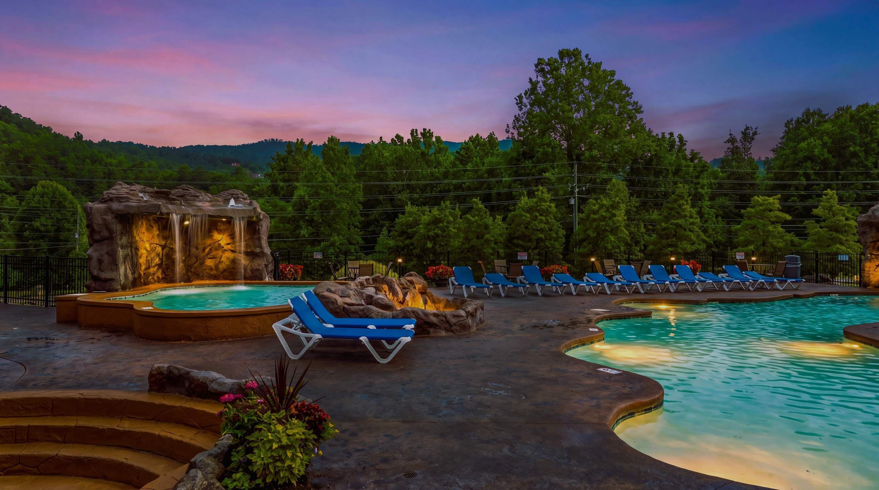 A pool area with lounge chairs, a hot tub, and a waterfall feature.