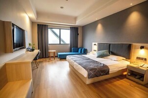 Una habitación de hotel moderna con una cama grande, un escritorio, un televisor y una ventana con cortinas.