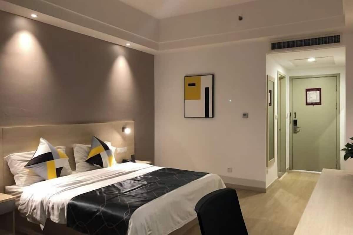 A modern hotel room with a bed, bedside table, and a door leading to a hallway.