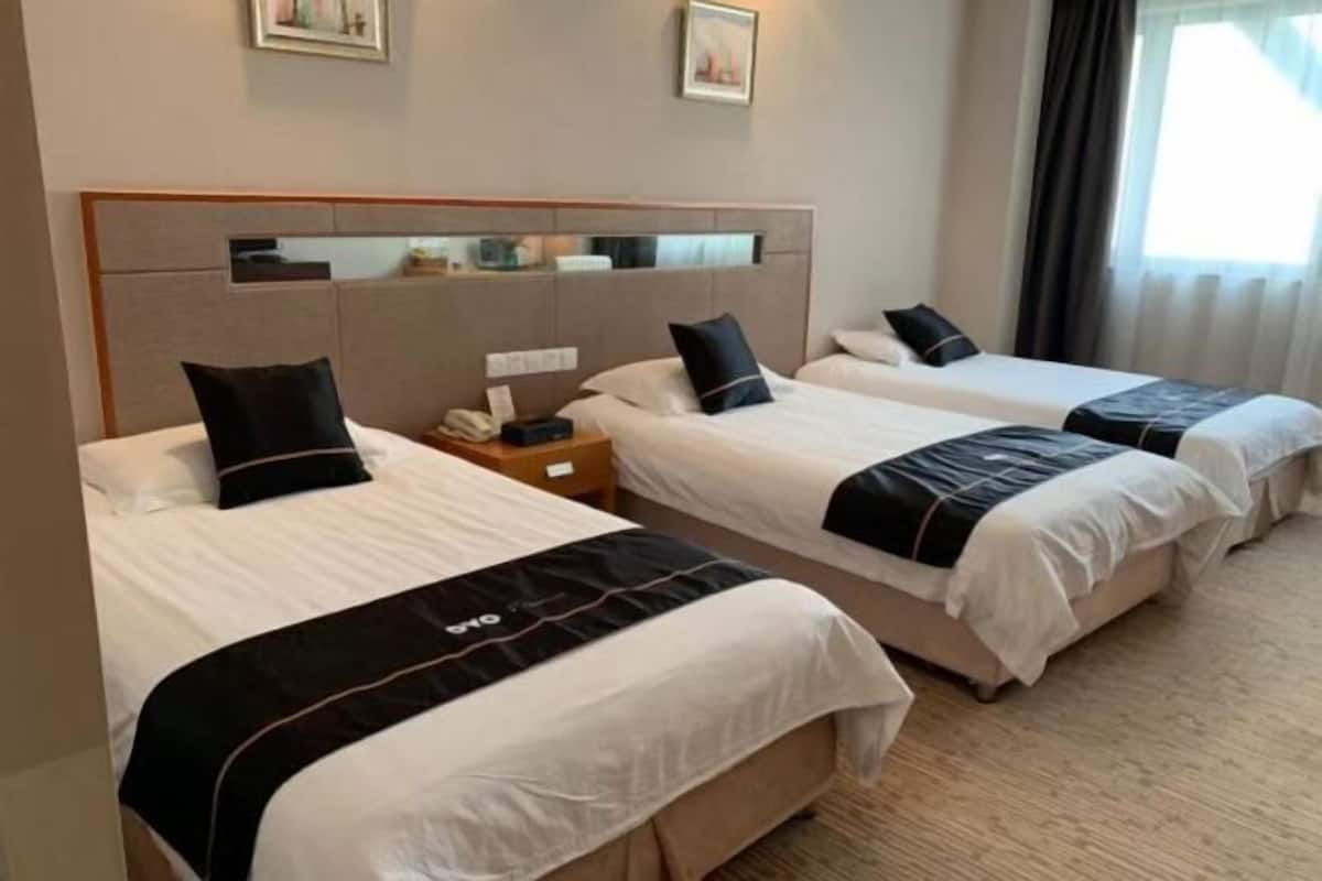 A hotel room with three beds, each with a black and white bedspread, a wooden headboard, and a bedside table with a lamp.