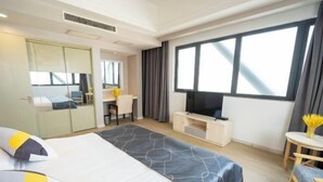 A hotel room with a large bed, a desk with a TV, a small table with a vase, and a window with curtains. - Zexi Business Hotel (Taicang)