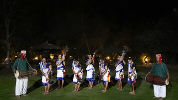 Un grupo de personas vestidas con trajes tradicionales actuando en un escenario al aire libre sobre césped, de noche.