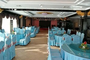 A banquet hall with round tables and chairs, a stage, and a large screen. - Hotel Intime Burqin (Burqin)