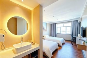 Una habitación de hotel con un espejo grande y redondo, un lavamanos, una cama, un escritorio y un televisor.