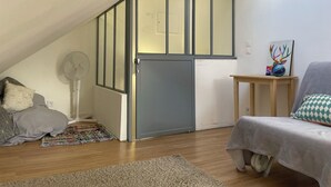 Ein Zimmer mit schrägen Wänden, Holzboden, grauem Sofa, kleinem Holztisch und einer Tür mit Milchglasfenster.