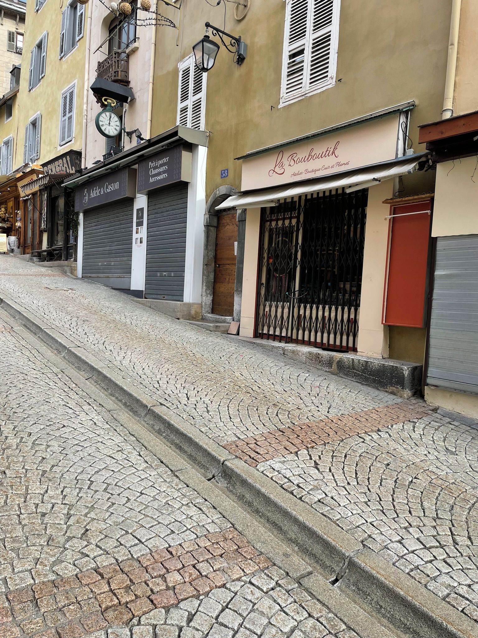 A cobblestone street with closed storefronts, including a boutique and a general store.