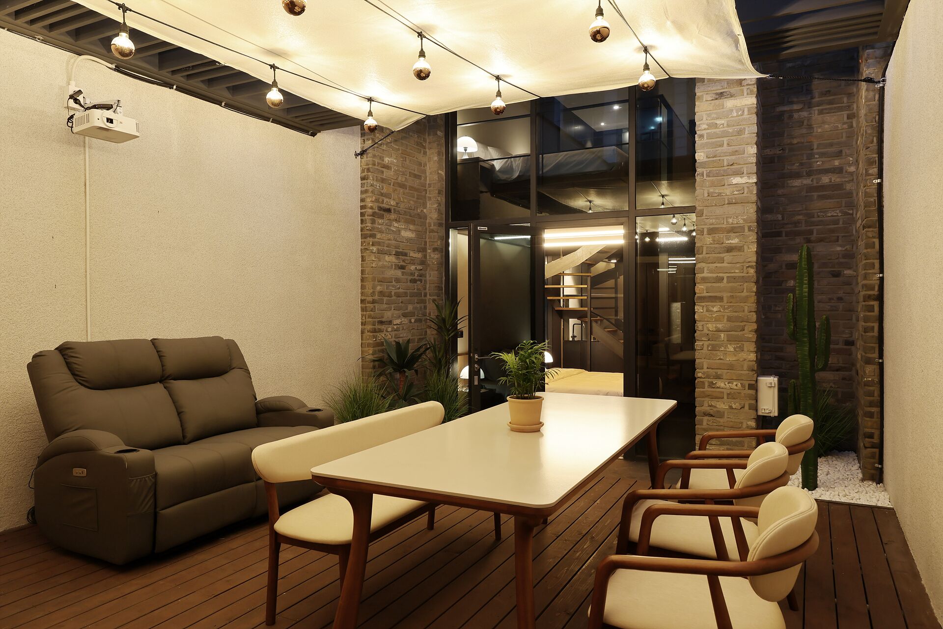 A patio with a sofa, table, and chairs, a projector, and a brick wall.