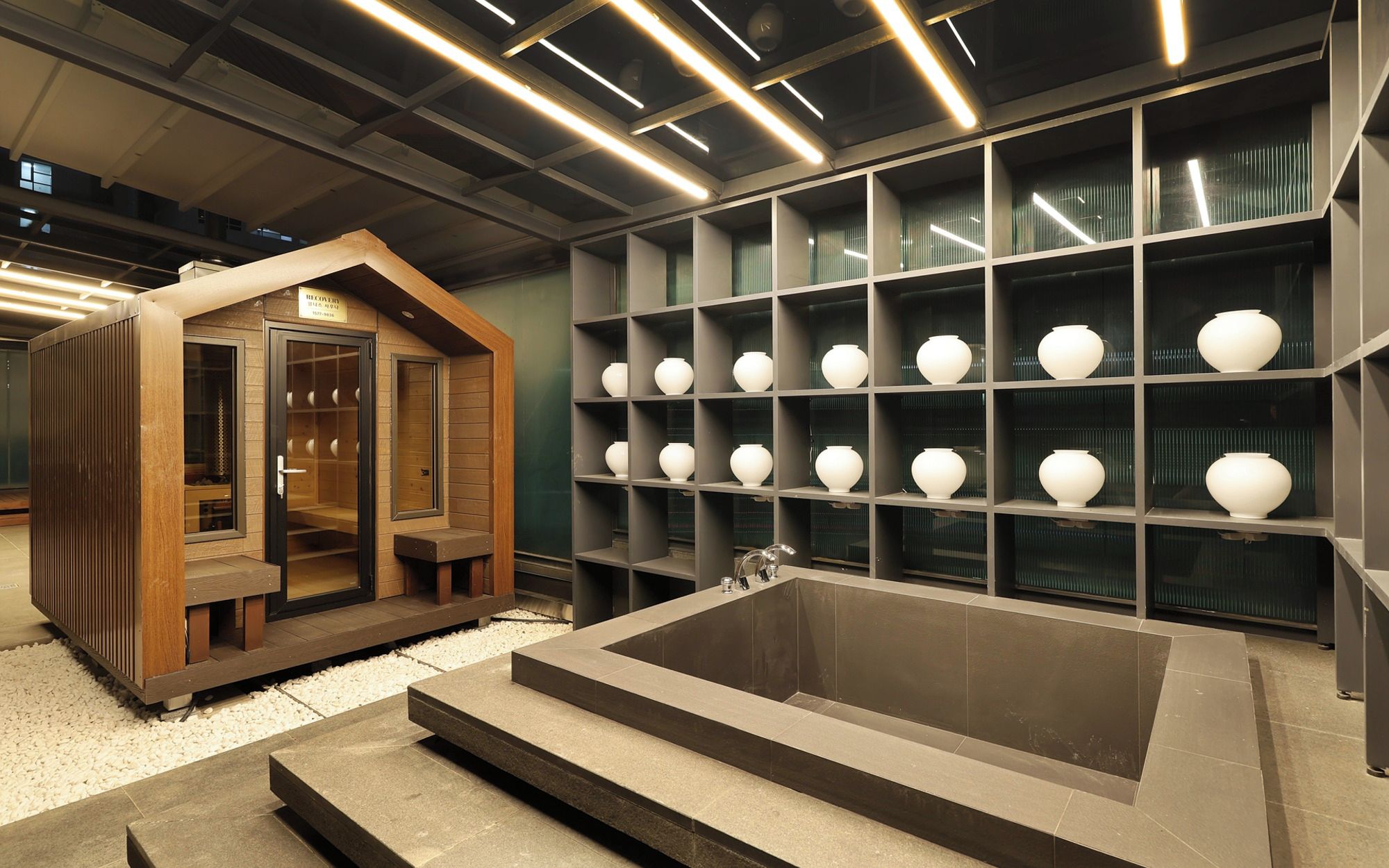 Un baño moderno con una bañera grande, repisas con jarrones blancos y una estructura de madera con puertas de vidrio.