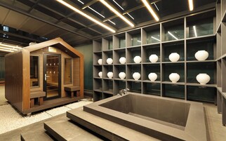 Un baño moderno con una bañera grande, repisas con jarrones blancos y una estructura de madera con puertas de vidrio.