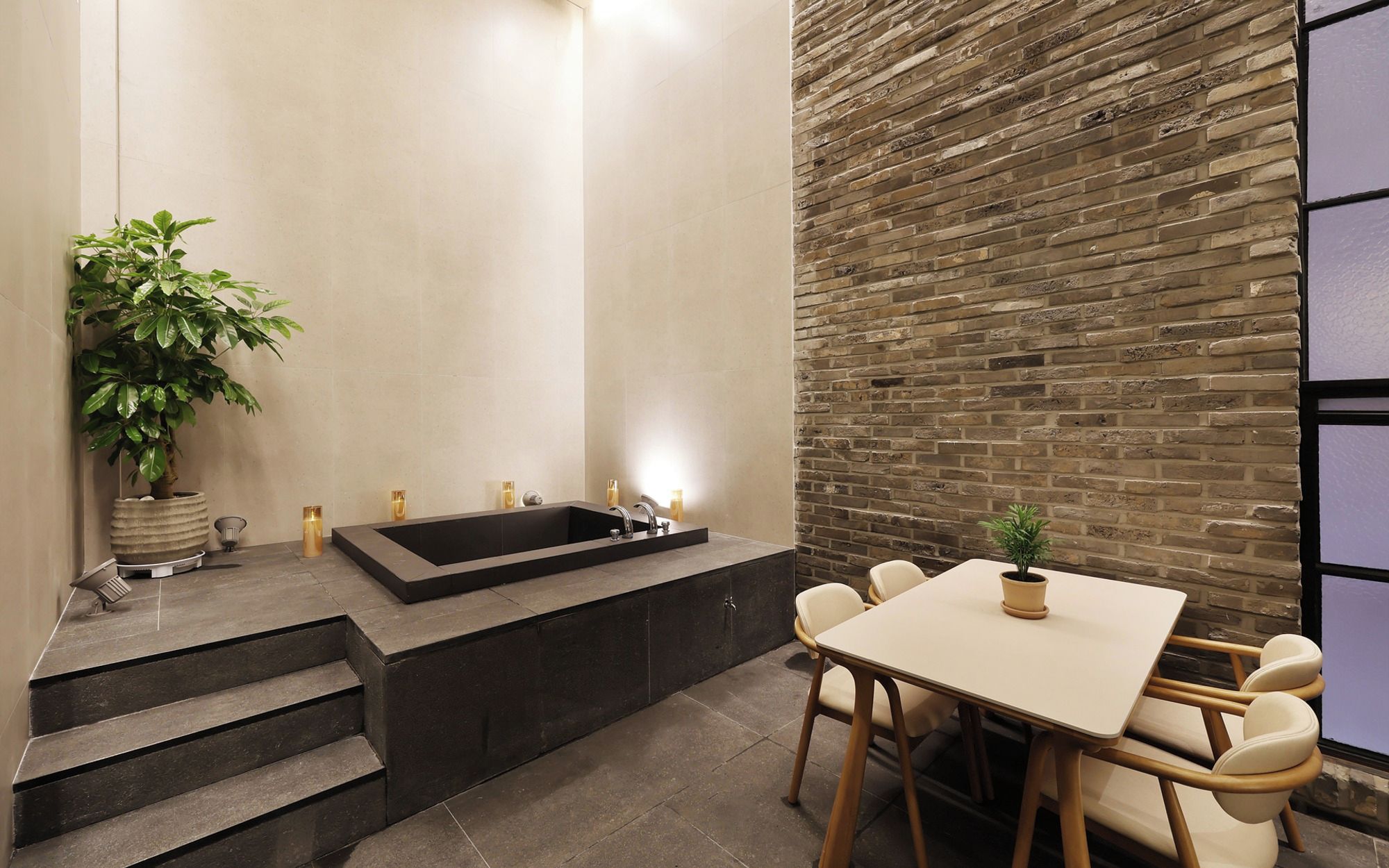 A modern bathroom with a large bathtub, a sink, and a potted plant. There are steps leading up to the bathtub and a table with chairs in the foreground.