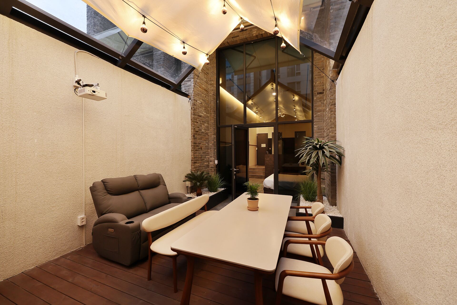 A modern patio with a dining table, chairs, a sofa, and a potted plant.