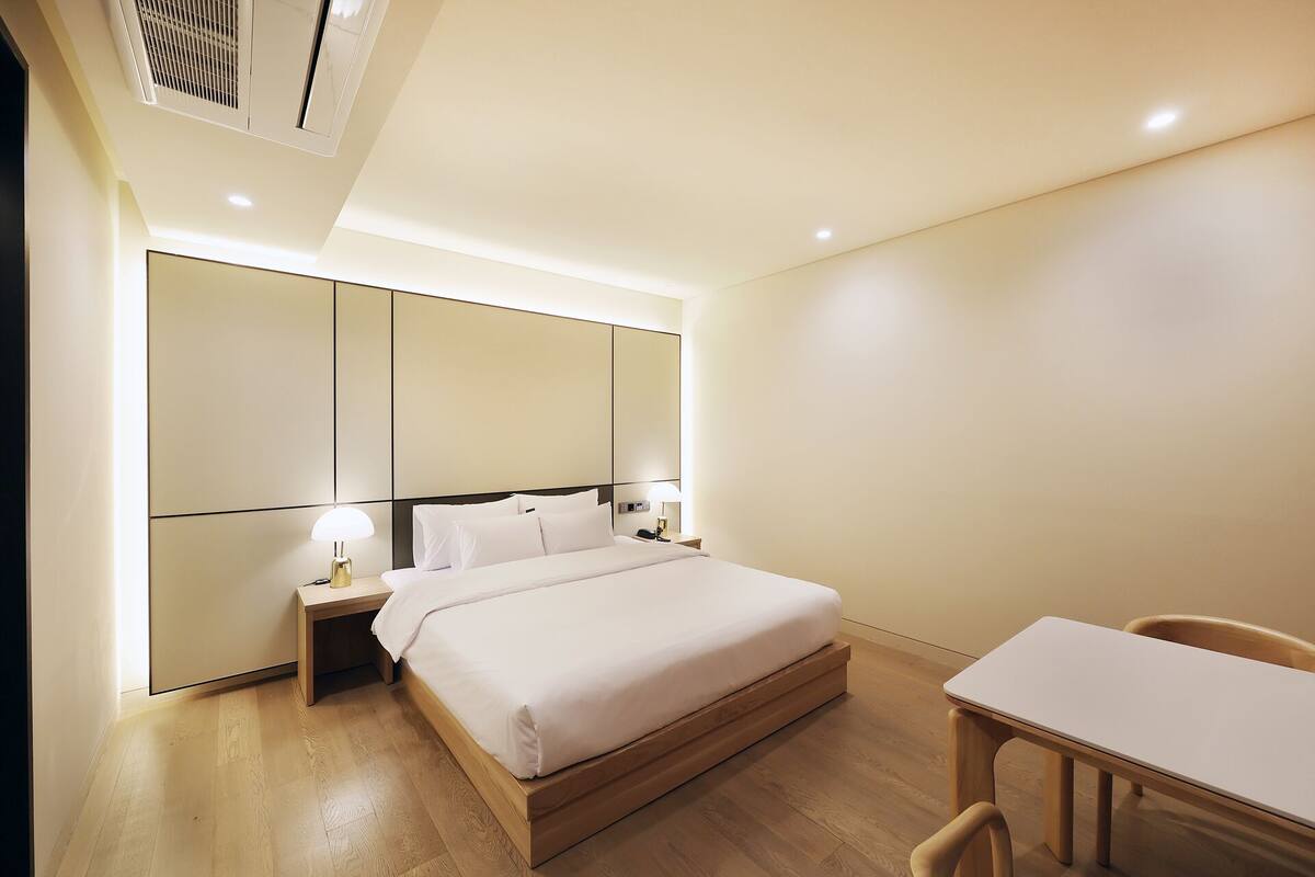 A hotel room with a bed, bedside lamps, a desk, and a chair.