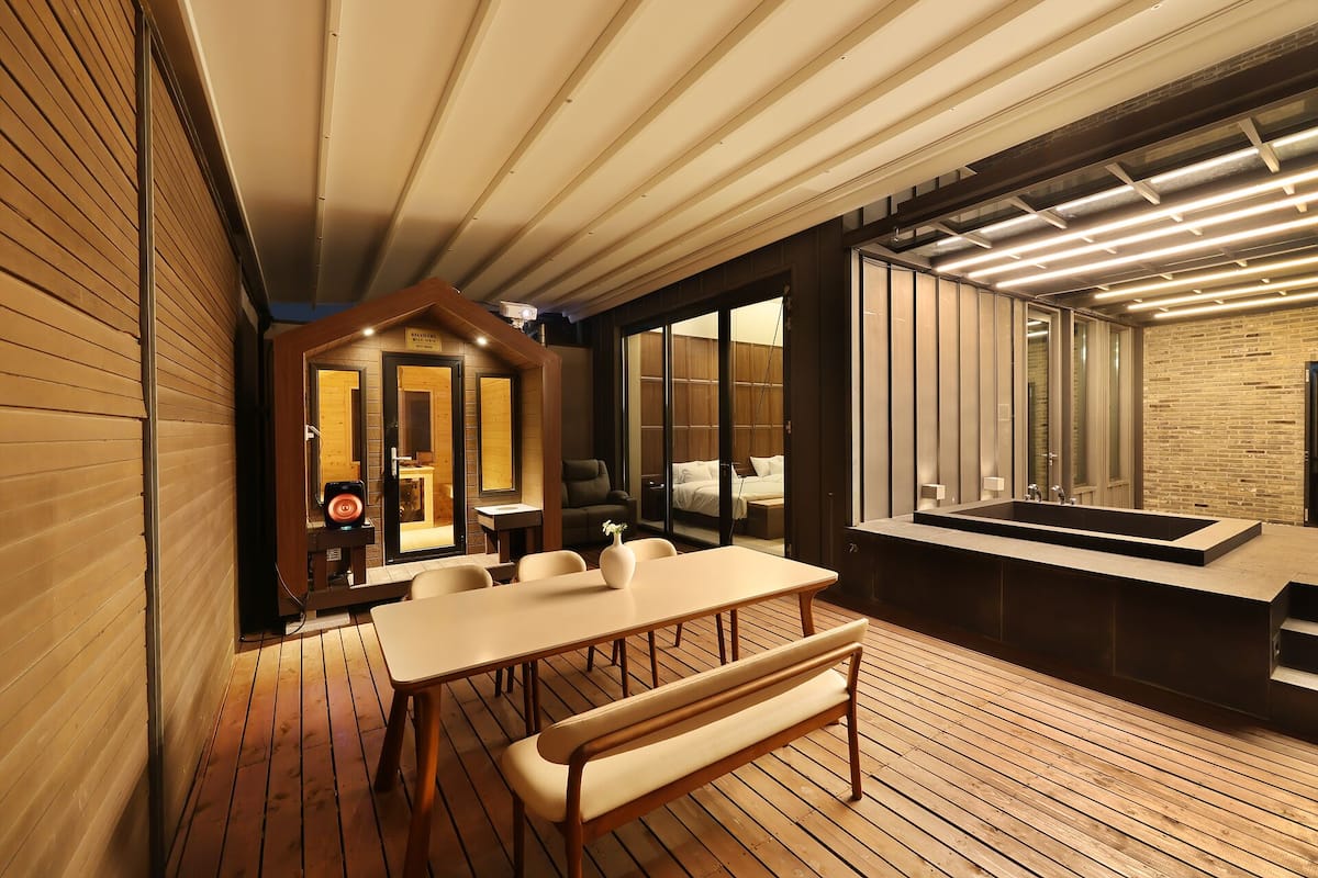 A modern interior with a wooden deck, a dining area, a large window, and a spa-like room.