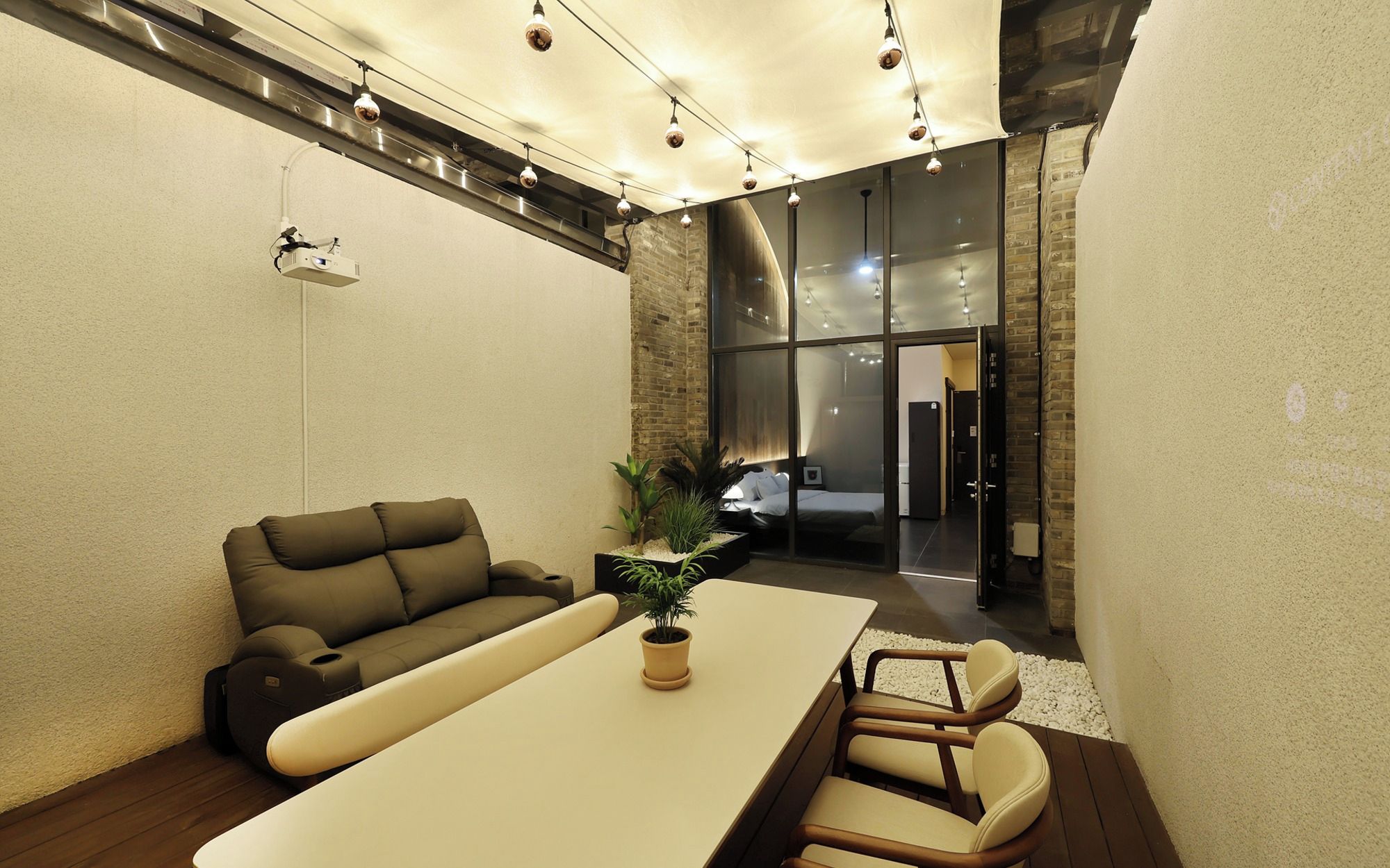 A modern interior with a sofa, a dining table, and chairs. There is a potted plant on the table.