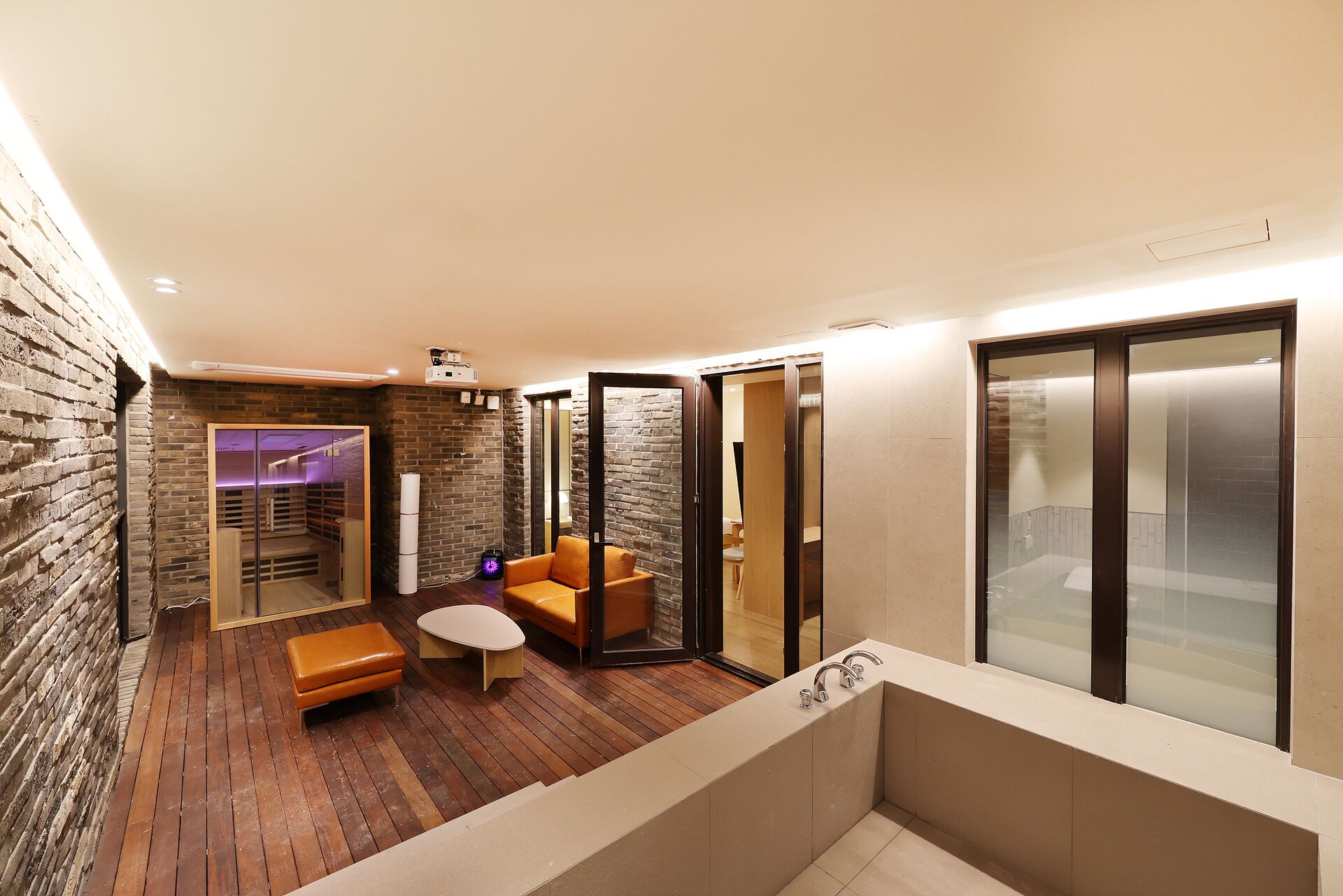 A modern interior with a wooden floor, a seating area with a table, and a glass-enclosed shower.