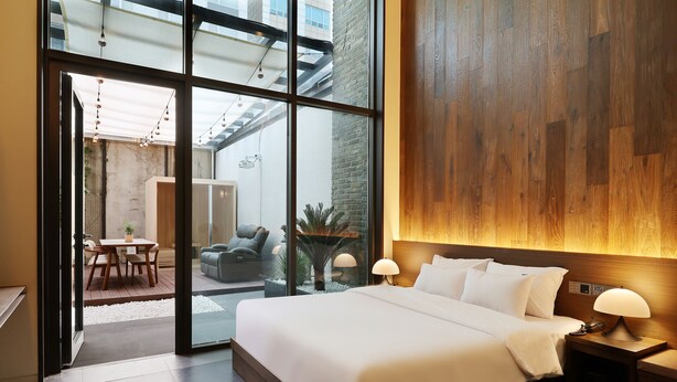 Una camera d'albergo moderna con un letto grande, una parete decorata in legno, una porta vetrata che dà su un'area esterna e un tavolino con sedie.