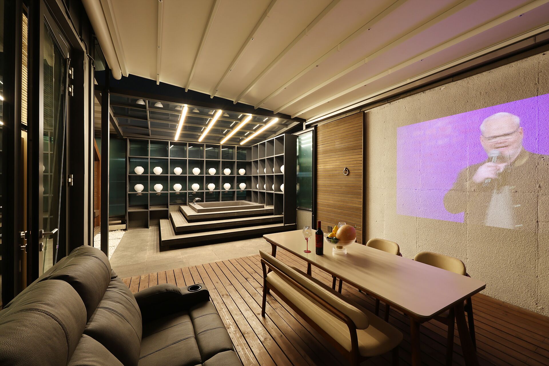 A modern interior with a sofa, a dining table, and a projection screen displaying a person.