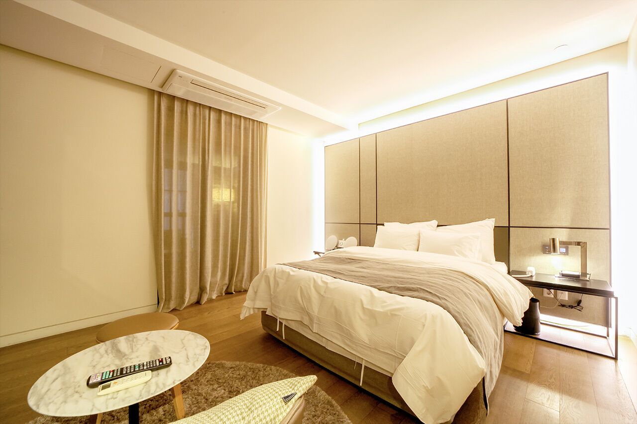 A hotel room with a bed, a bedside table, a remote control, a small table, and a window with curtains.