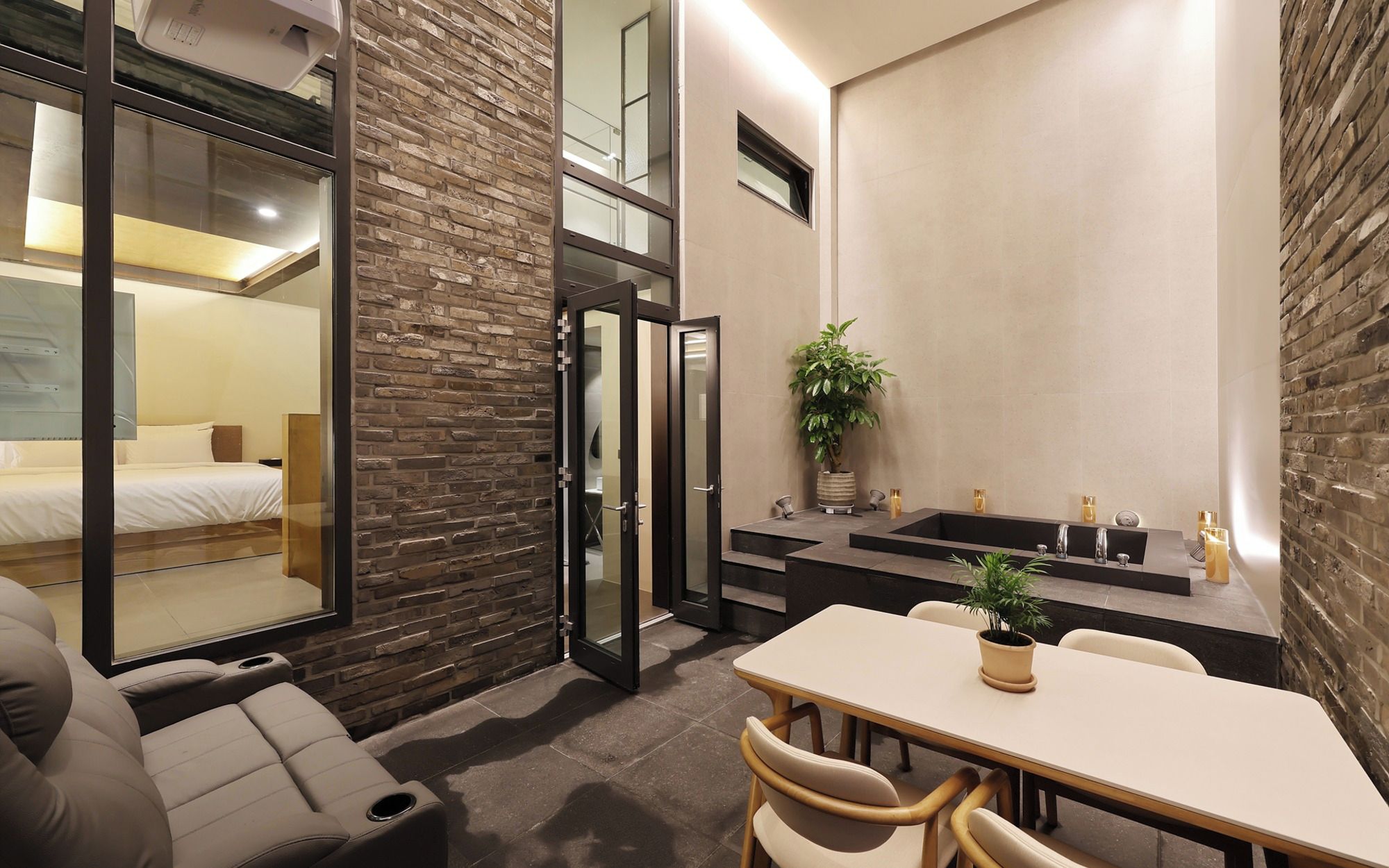 Una habitación de hotel moderna con cama, zona de estar y baño con lavabo y espejo.