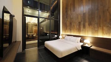 Habitación de hotel moderna con una cama grande, mesitas de noche, un revestimiento de pared de madera y una puerta de vidrio que da a un comedor.
