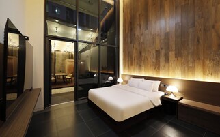 Habitación de hotel moderna con una cama grande, mesitas de noche, un revestimiento de pared de madera y una puerta de vidrio que da a un comedor.