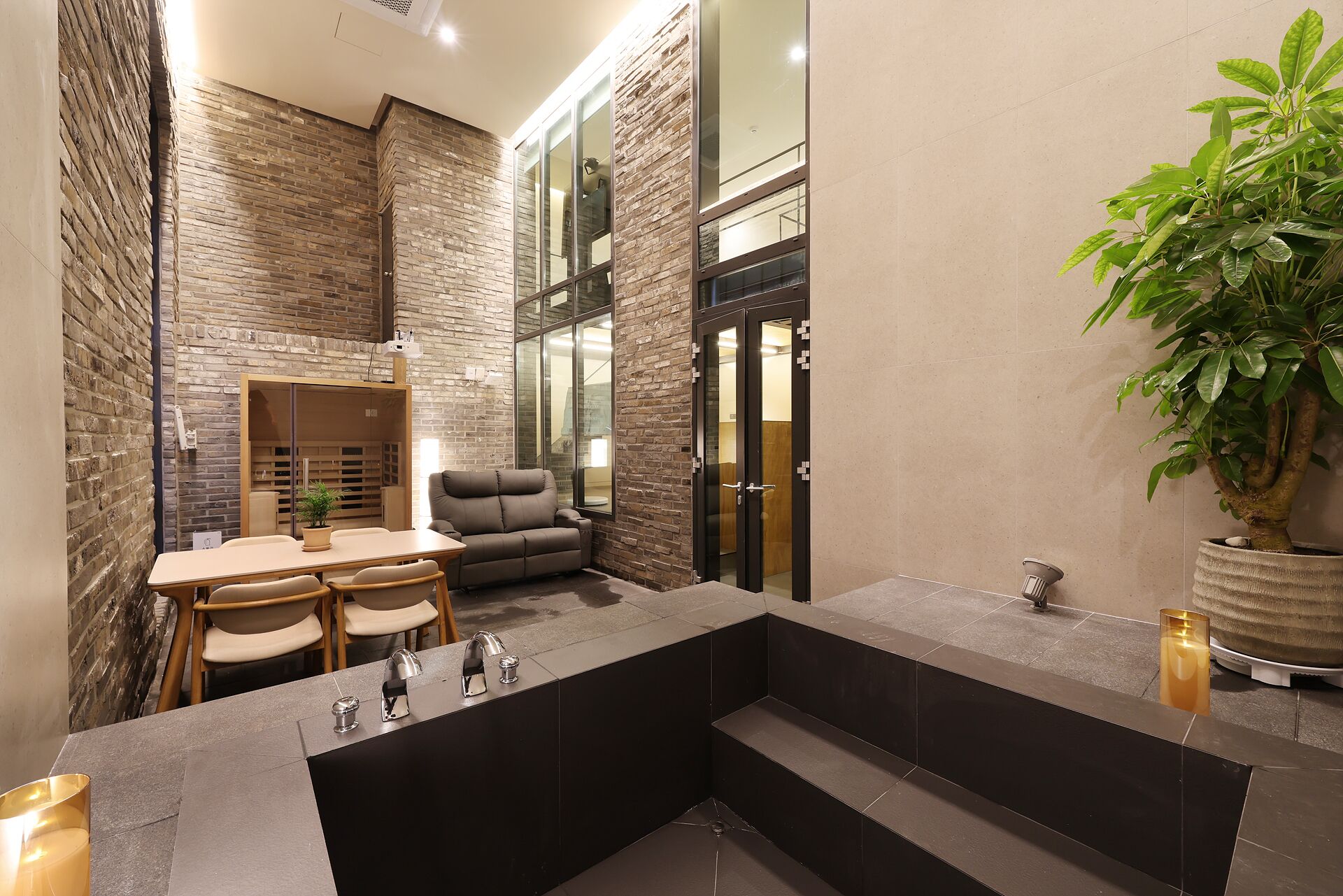 A modern bathroom with a stone wall, a seating area with a table and chairs, a large mirror, and a potted plant.