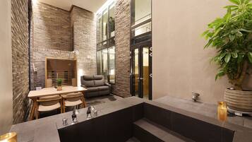 A modern bathroom with a stone wall, a seating area with a table and chairs, a large mirror, and a potted plant.