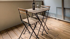 En balkong med ett träbord och stolar, en flaska vin och ett glas.