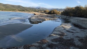 A coastal landscape with a sandy beach, calm water, and distant mountains.
