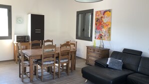 A dining area with a wooden table and chairs, a black sofa, a cabinet, and a painting on the wall.