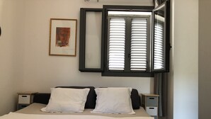 A bedroom with a bed, two bedside tables, a framed picture on the wall, and a window with blinds.