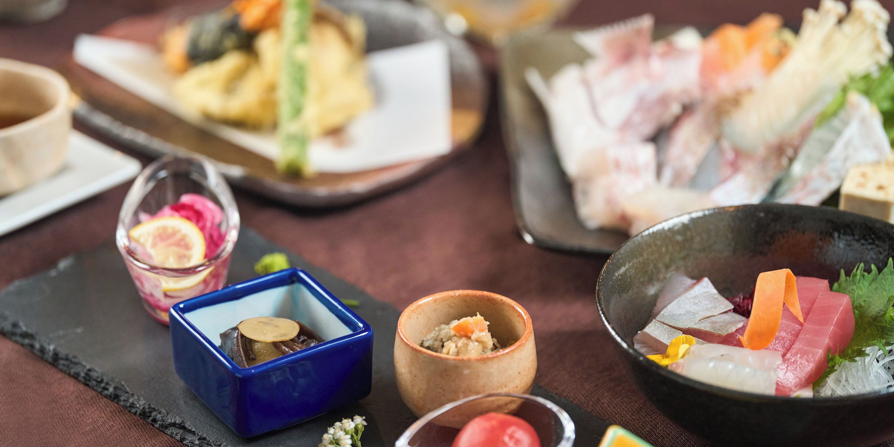 A variety of dishes, including sashimi and sushi, arranged on a table.