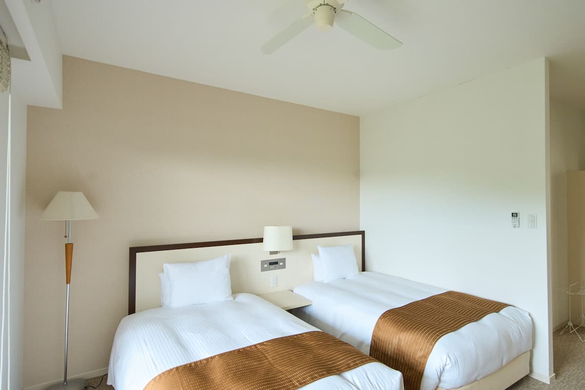 Una habitació d'hotel amb dos llits, un ventilador de sostre, una taula de nit amb una làmpada i un armari.