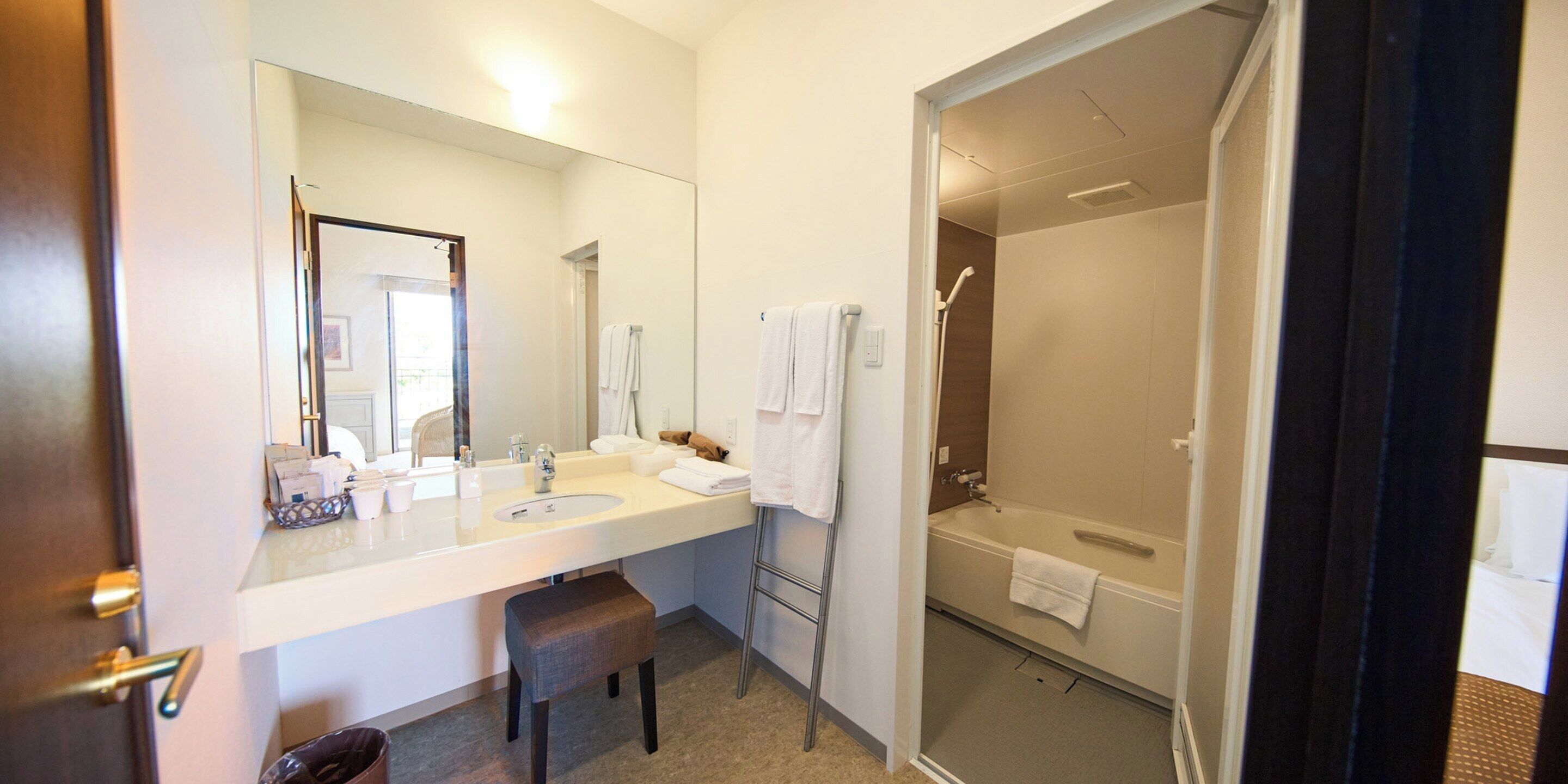 Een moderne badkamer met een grote spiegel, een wastafel, een douche en een bankje.
