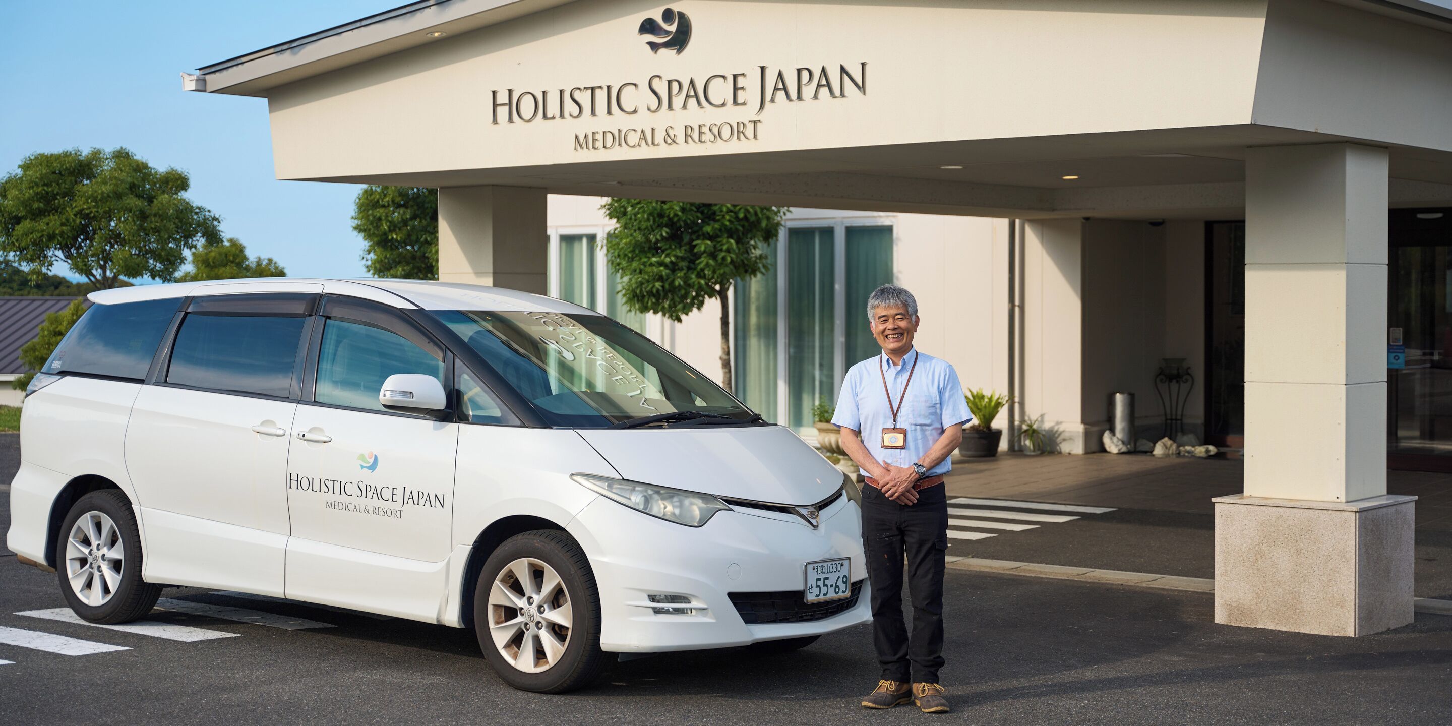 A white van parked in front of a building with a sign reading "Holistic Space Japan Medical & Resort."