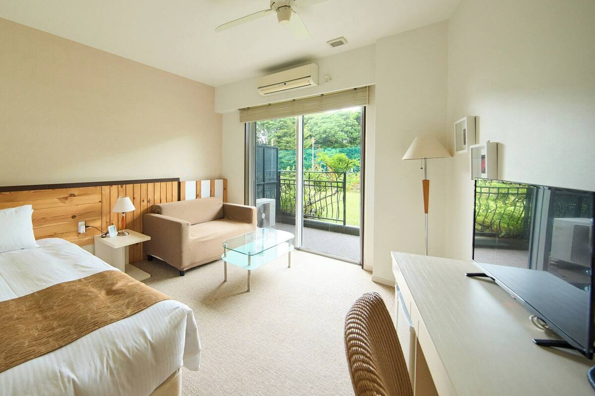 A hotel room with a bed, a sofa, a glass coffee table, a desk, and a TV.