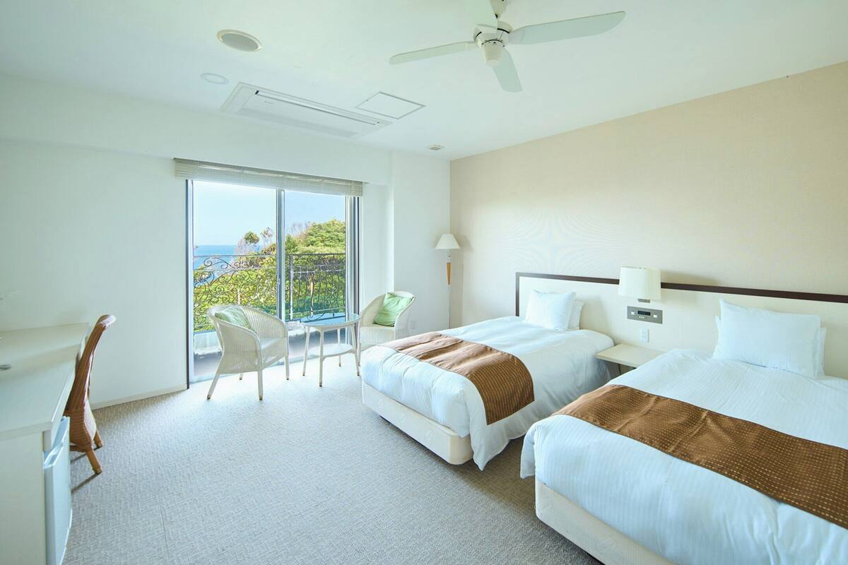 A hotel room with two beds, a TV, a desk, and a balcony with a view.