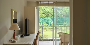 Relax in a stylish room with a flat-screen TV, desk, and wicker chair, plus a balcony overlooking a serene garden.