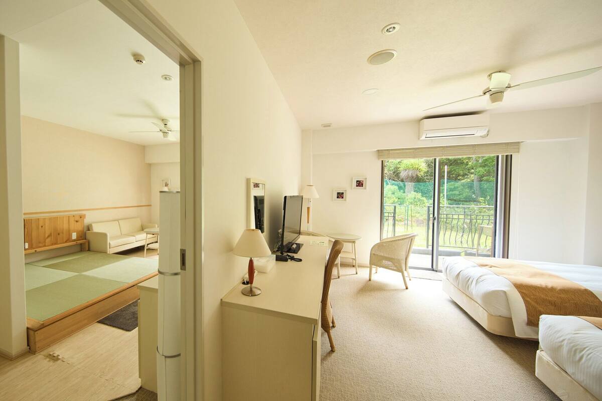 A hotel room with a bed, a desk, a chair, a sofa, and a view of the outdoors.