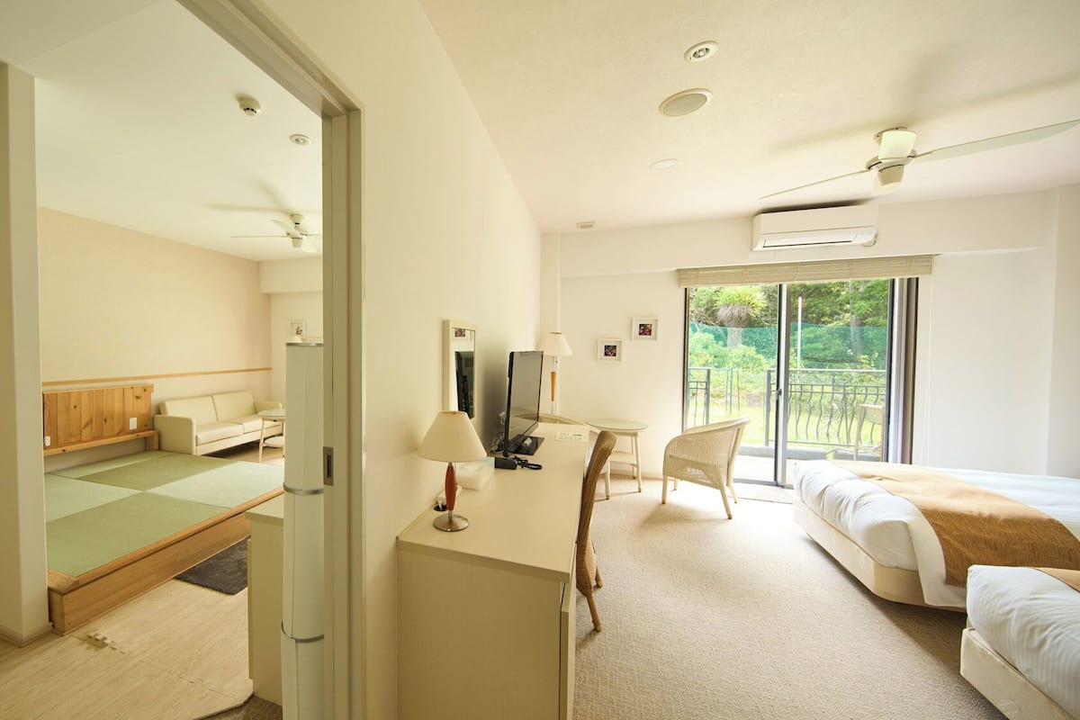 A hotel room with a bed, a desk, a chair, a sofa, and a view of the outdoors.