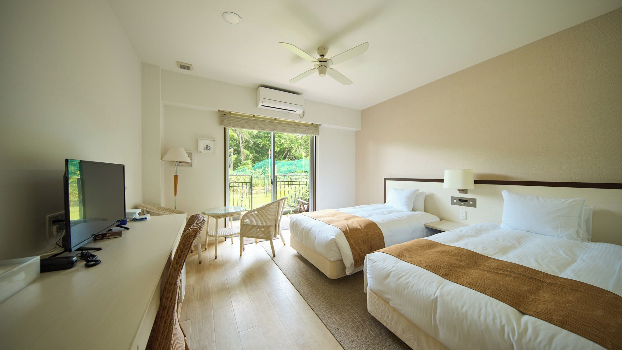 A hotel room with two beds, a desk with a TV, a chair, a ceiling fan, and a view of the outdoors.