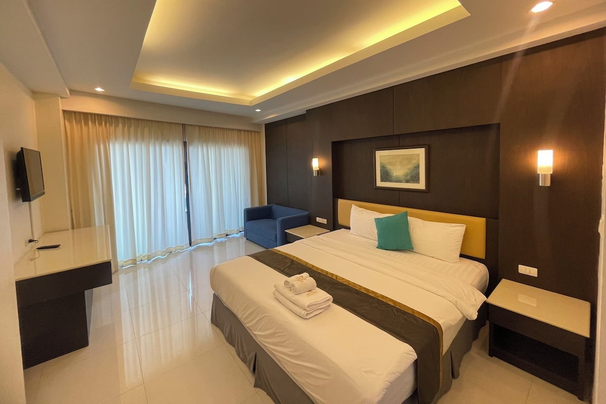 A hotel room with a large bed, a desk, a chair, and a TV.