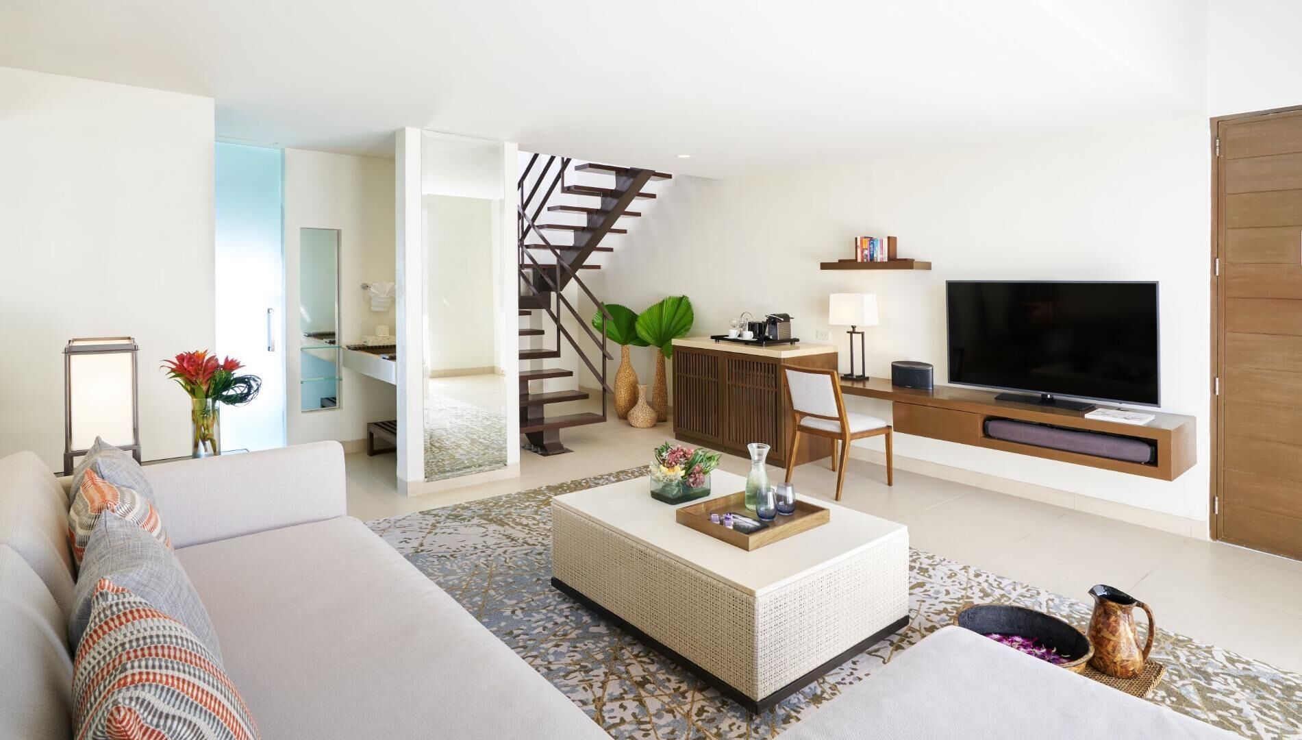 Una sala moderna con sofá, mesa de centro, televisor y una escalera que lleva a un dormitorio.