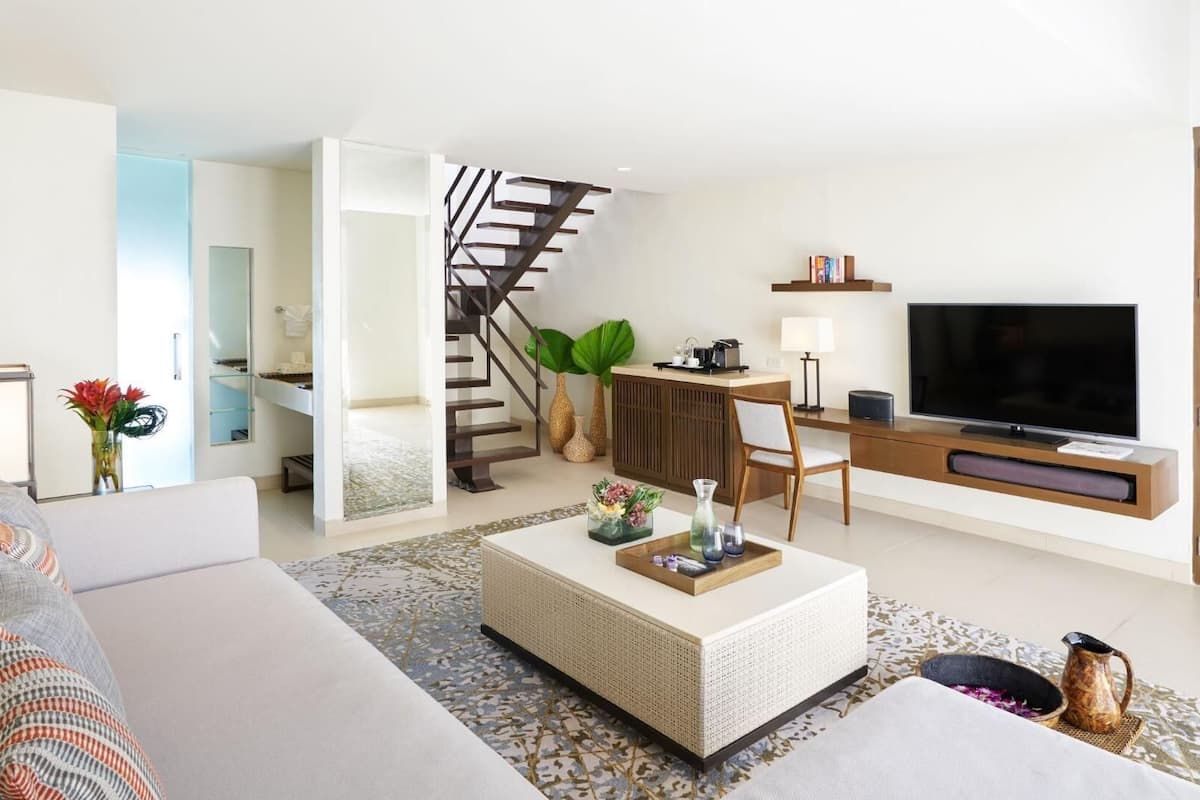 A modern living room with a sofa, coffee table, TV, and a staircase leading to a bedroom.