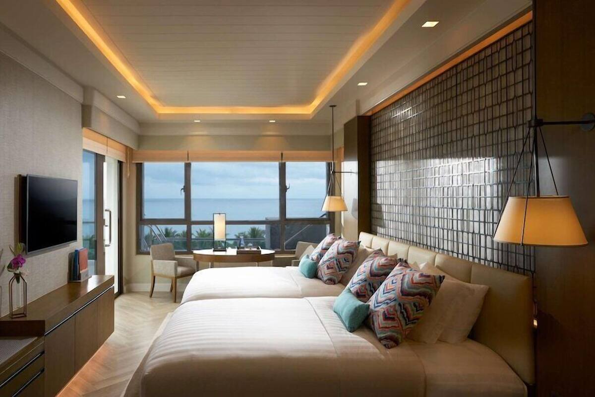 A hotel room with a bed, a TV, a desk, and a view of the ocean.